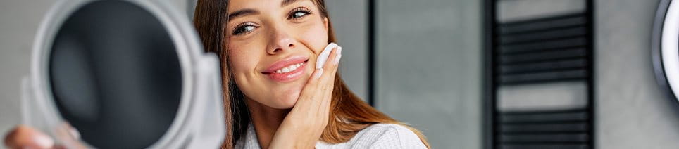 Frau sieht sich in den Spiegel und reinigt das Gesicht