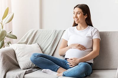 Schwangere Frau hält den Babybauch und sitzt auf dem Sofa