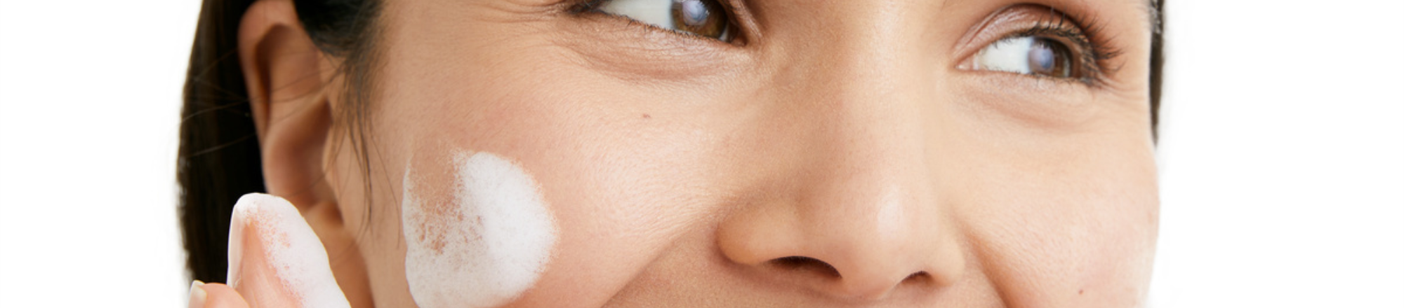 Woman smiling and applying face cream on a white background