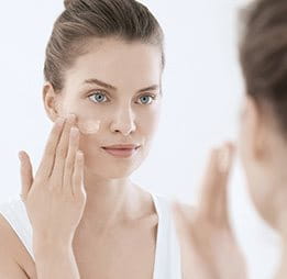 Woman applying skincare in the mirror