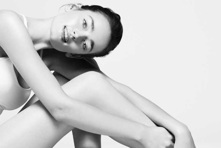 Black-and-white photo of a woman sitting with her knees drawn up and arms resting across them.