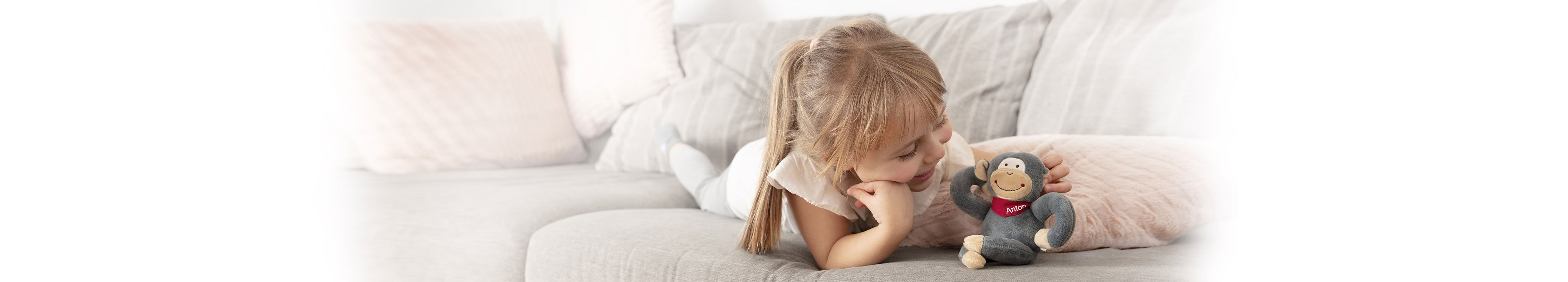 bambina stesa sul divano che gioca con pupazzo scimmia 