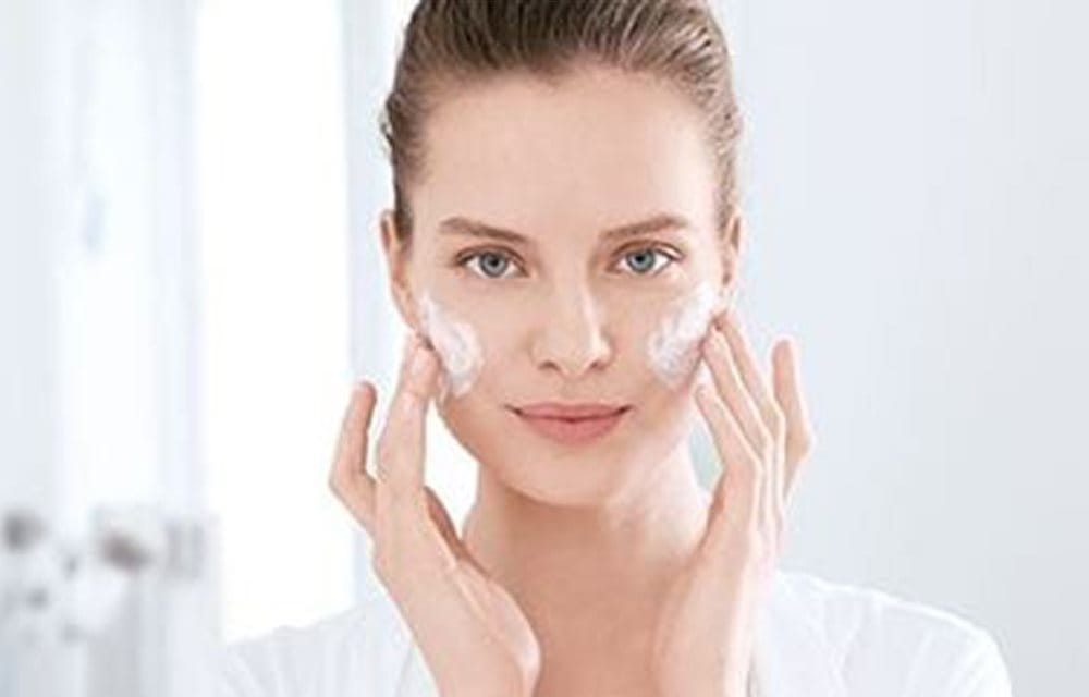 A woman cleansing her face before applying make-up on acne prone skin - Eucerin
