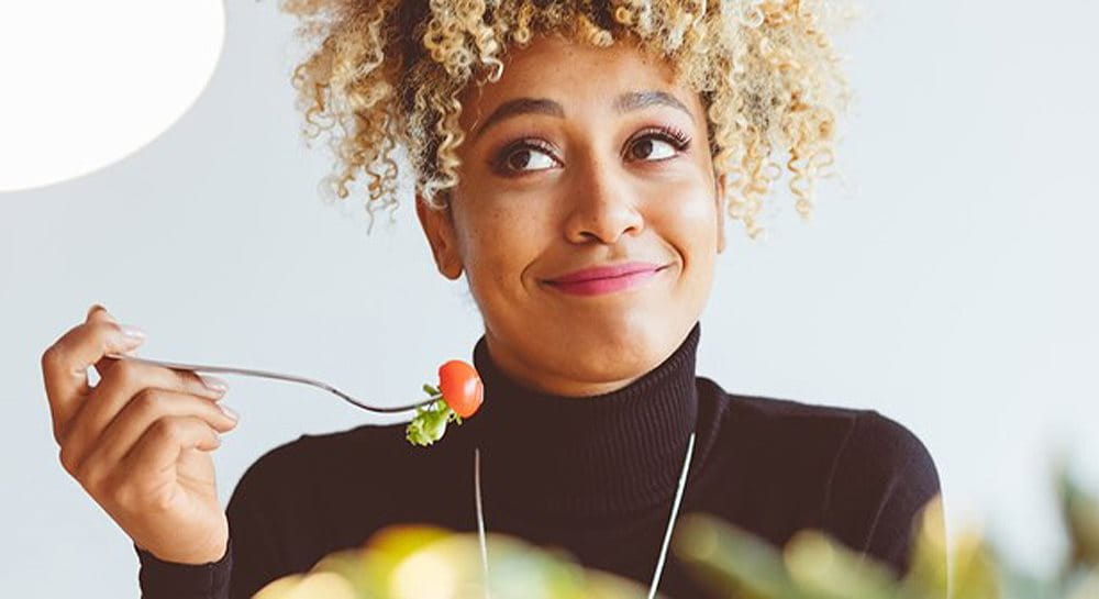 A woman eating a cherry tomato to fight acne - Eucerin