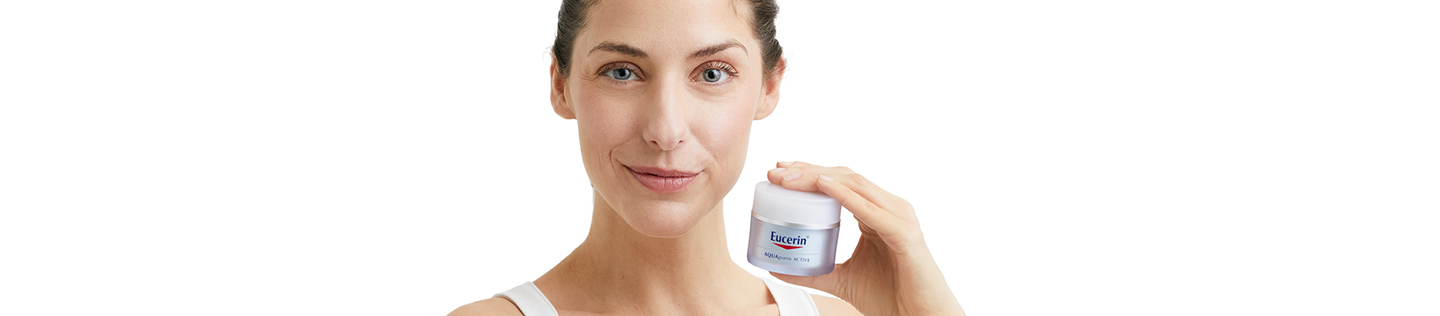 Темноволосая женщина держит в руке баночку крема Eucerin