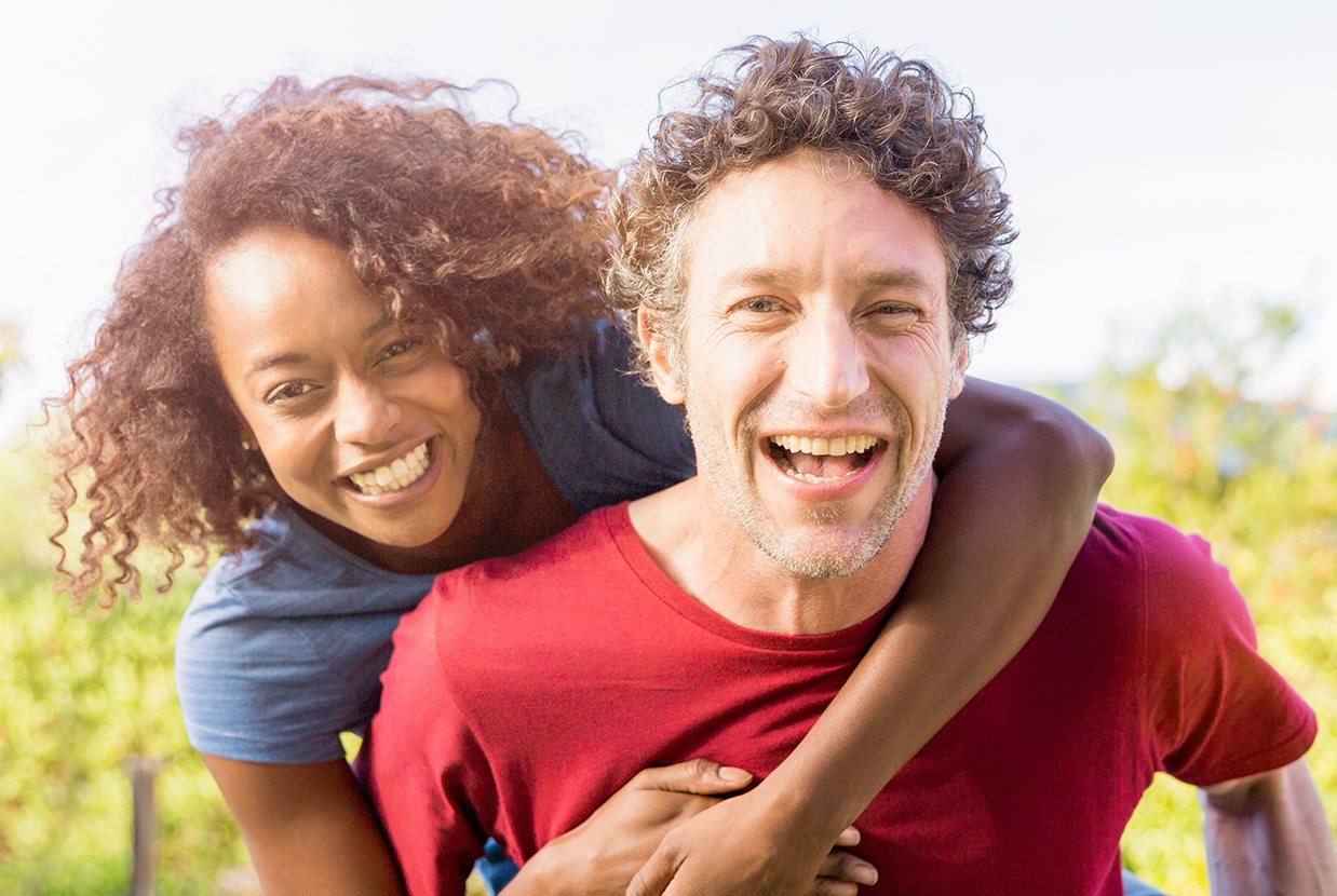 A woman happily piggybacks on a smiling man