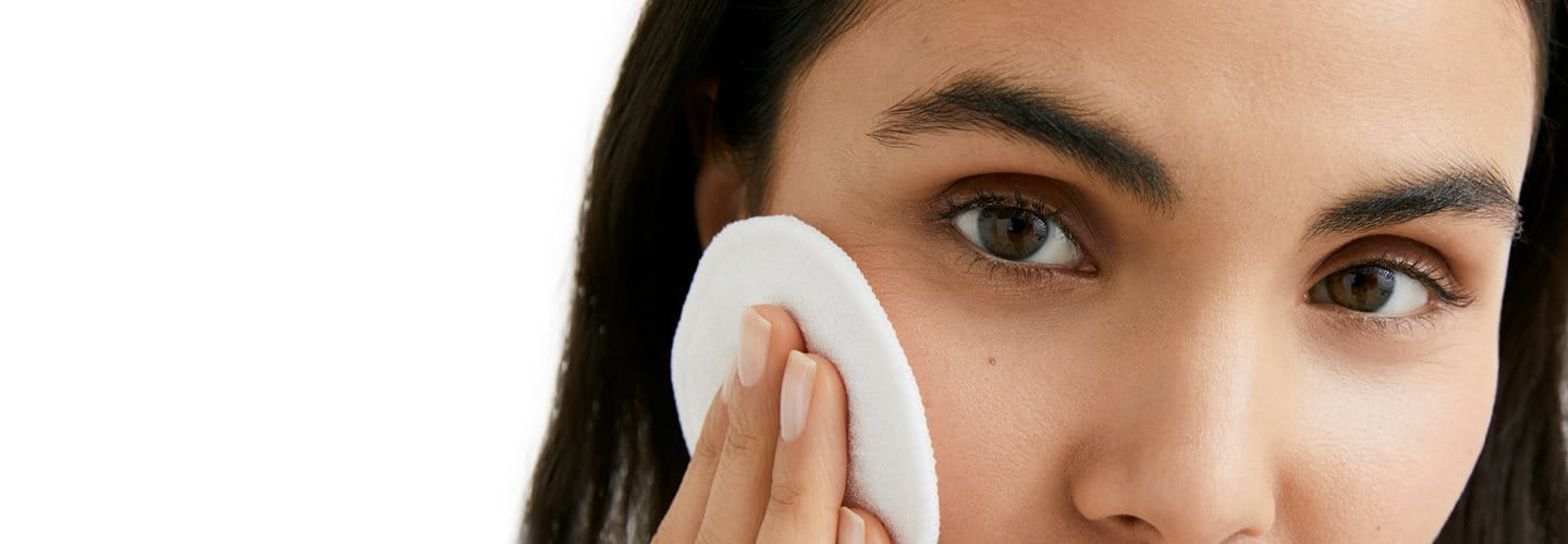 Woman using cotton pad on face for skincare routine.