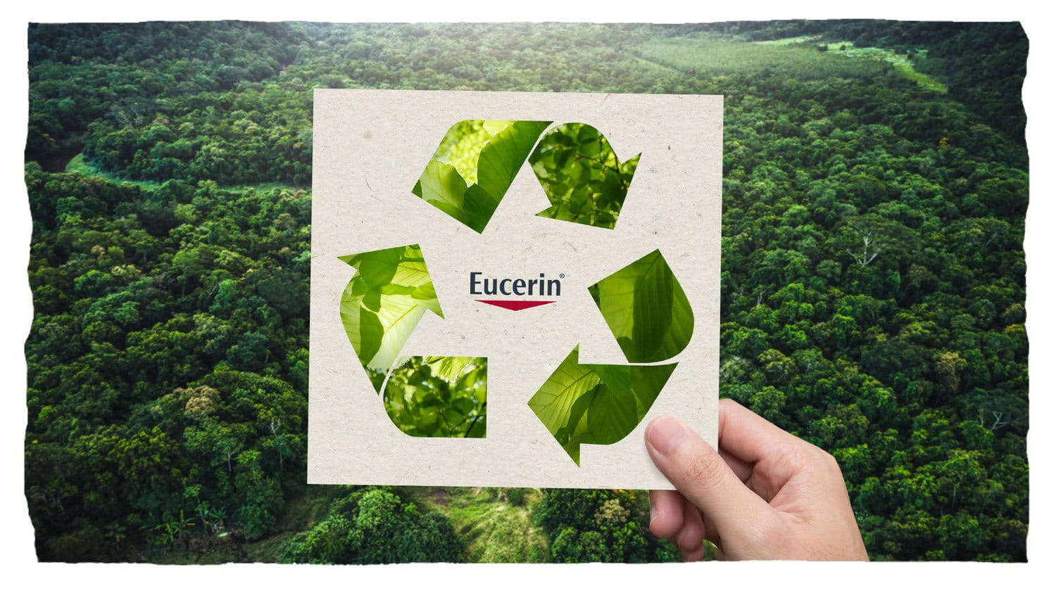 Hand holding a recycling symbol in front of a lush forest background.