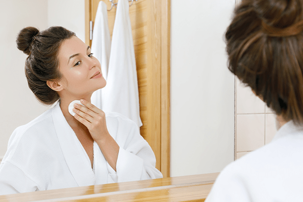 Femme devant un miroir tamponnant son cou avec un coton.