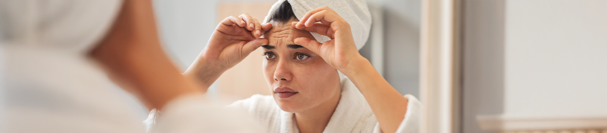 Frau am Spiegel berührt Falten auf der Stirn