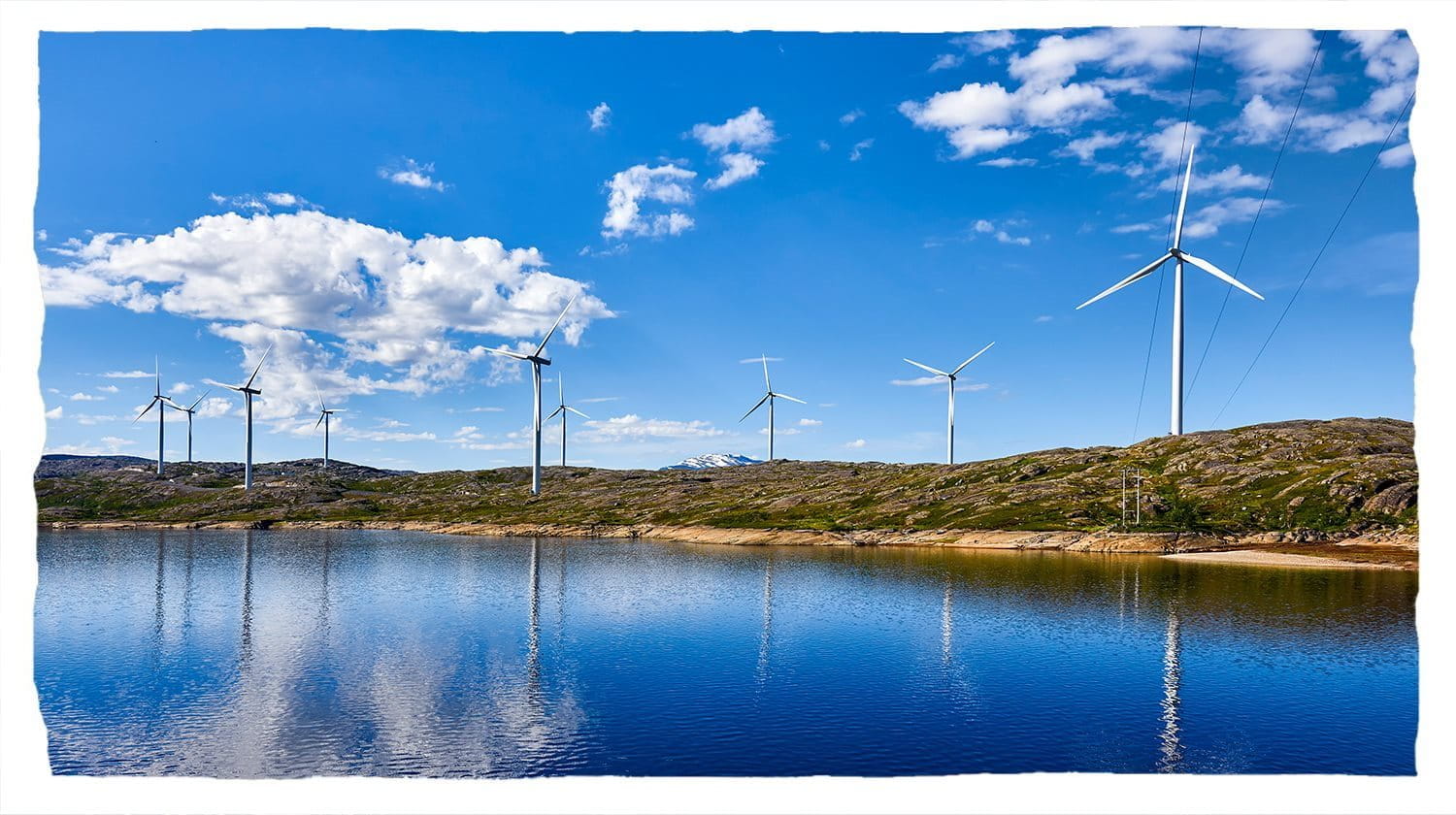 Éoliennes visibles sur les collines bordant un lac.