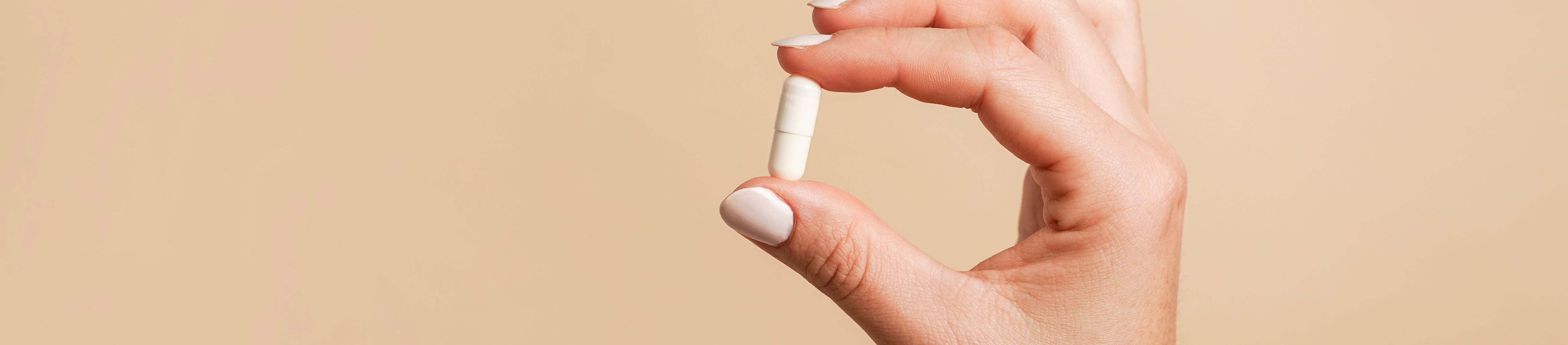 Nahaufnahme einer Hand, die eine Tablette hält vor einem braunen Hintergrund.