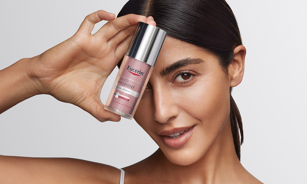 A picture of a woman with glass skin holding an Anti pigment dual serum
