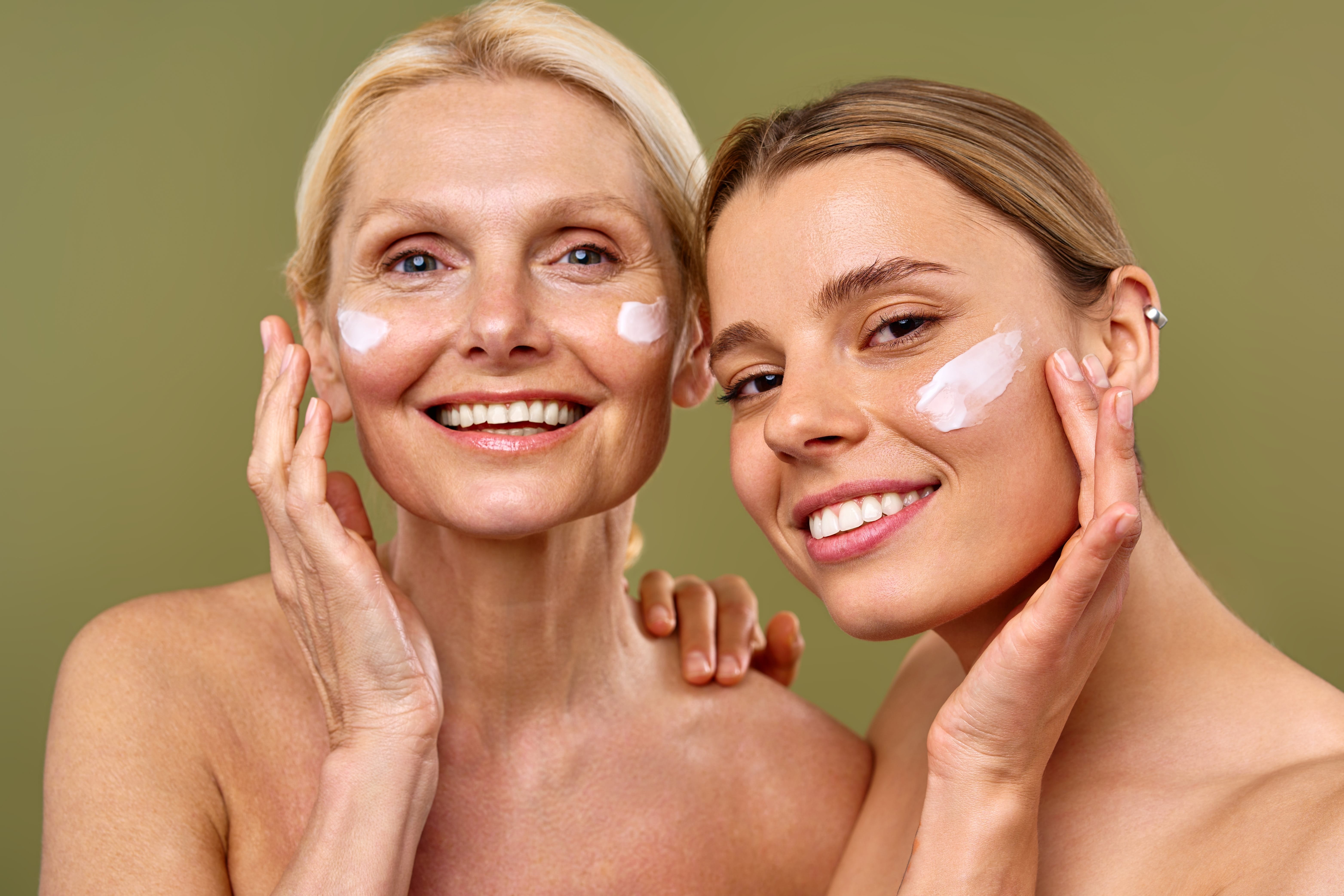 Eine Frontalaufnahme einer älteren und eine jüngeren Frau, die lachen und sich Ihr Gesicht mit einer Lotion eincremen.