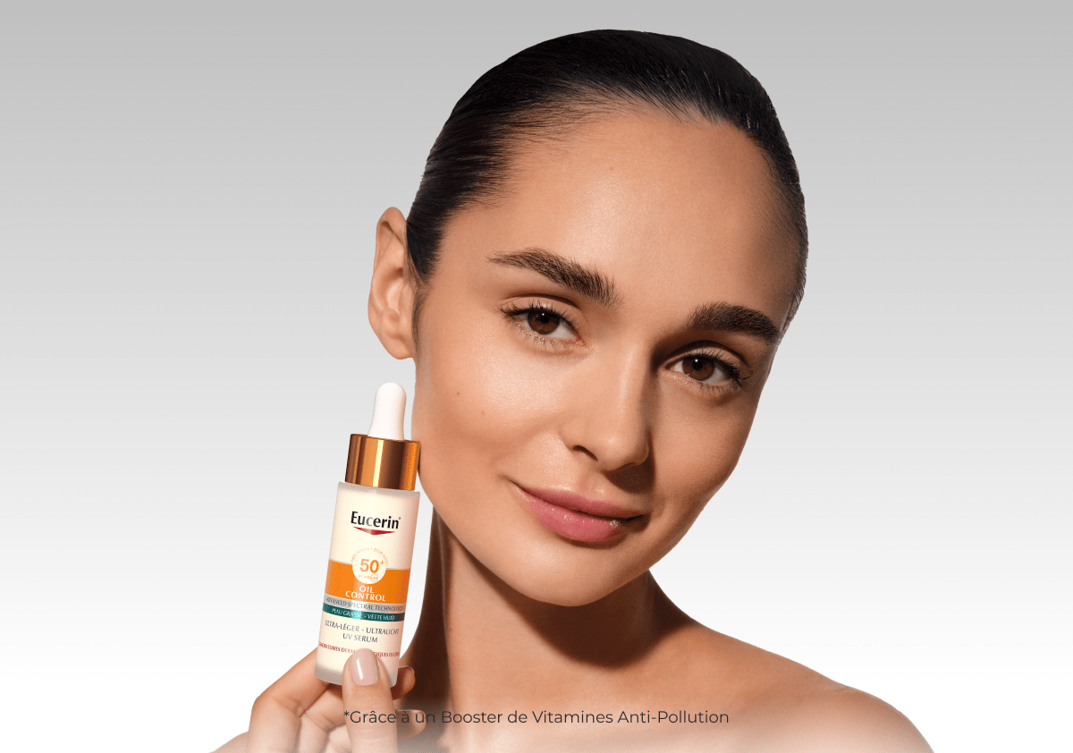 Une femme tenant le SUN Face Oil Control Sérum SPF 50+ d’Eucerin