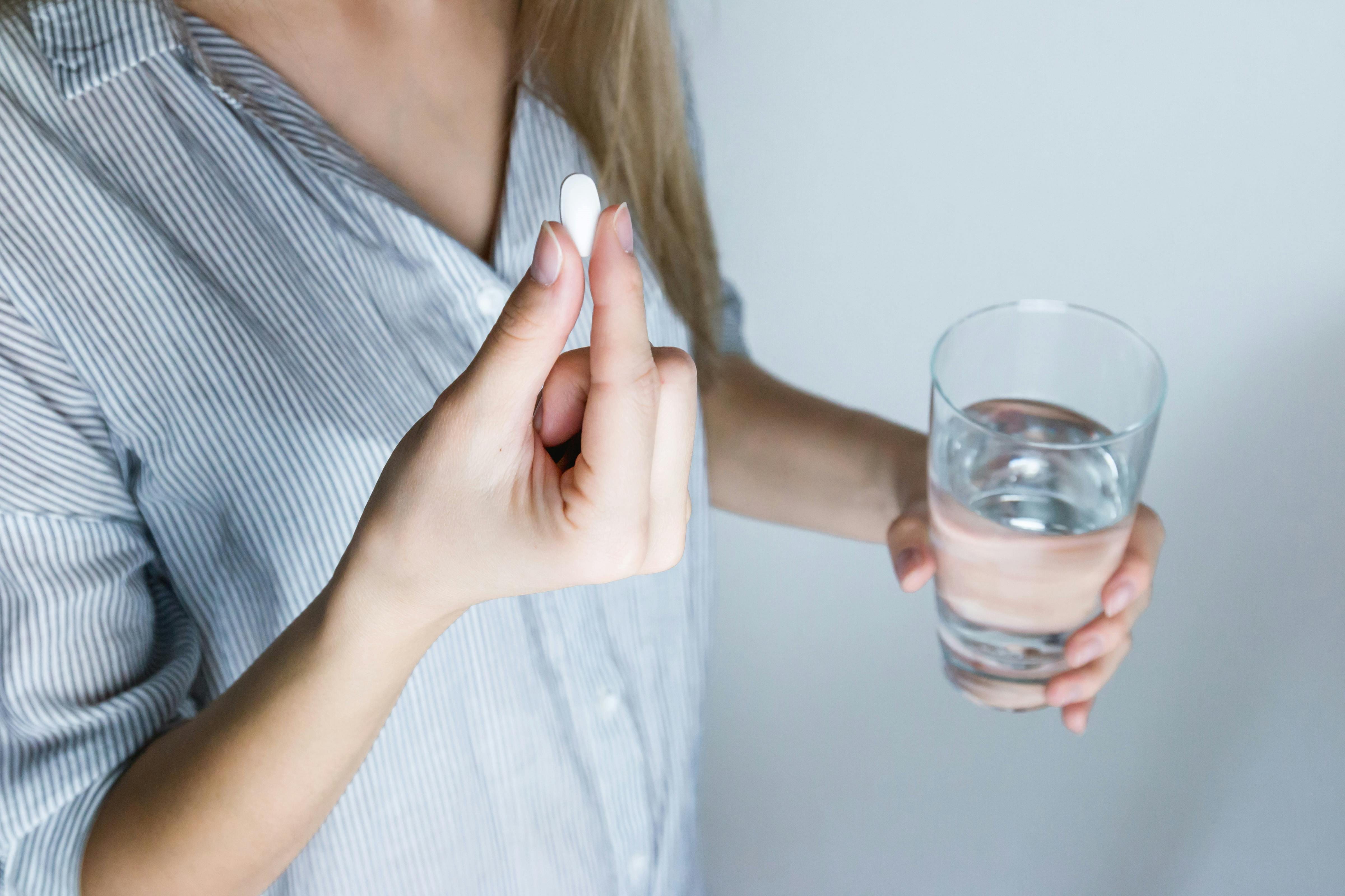 Eine Frau hält eine Tablette in der einen und ein Wasserglas in der andere Hand.