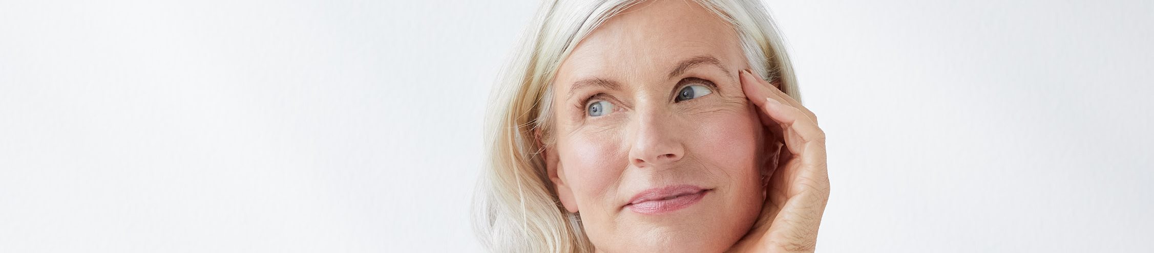 een vrouw die glimlacht en haar gezicht aanraakt, tegen een grijze achtergrond