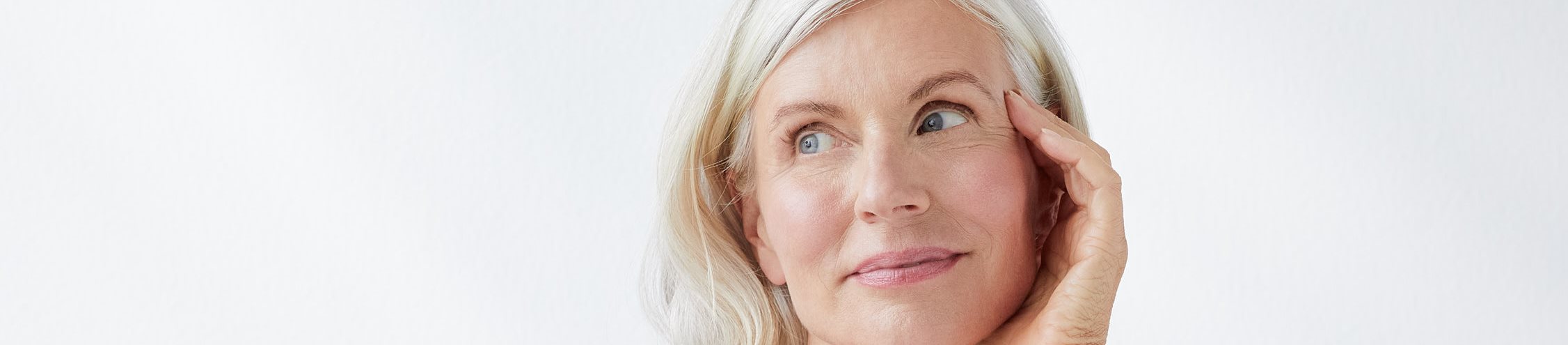 een vrouw die glimlacht en haar gezicht aanraakt, tegen een grijze achtergrond