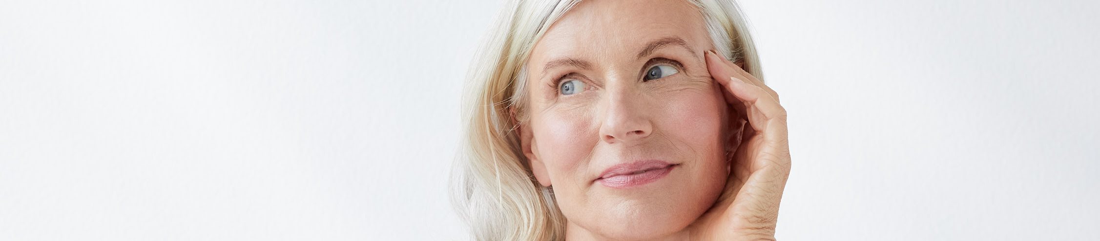 femme souriante qui se touche le visage, sur fond gris