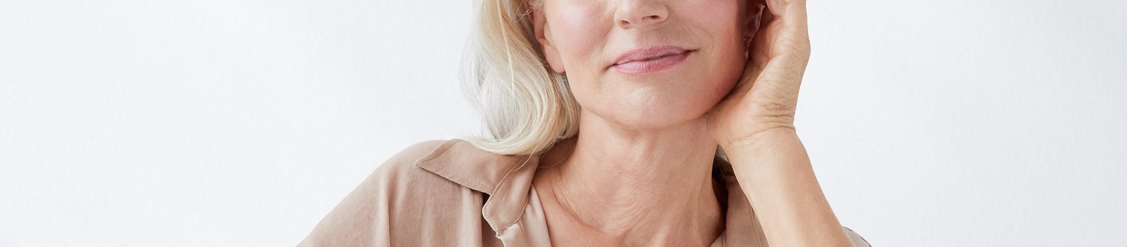 Eine Frau, die lächelt und ihr Gesicht berührt, vor einem grauen Hintergrund