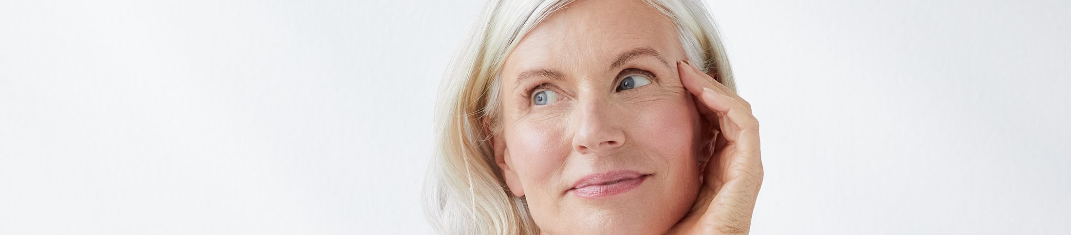 femme souriante qui se touche le visage, sur fond gris