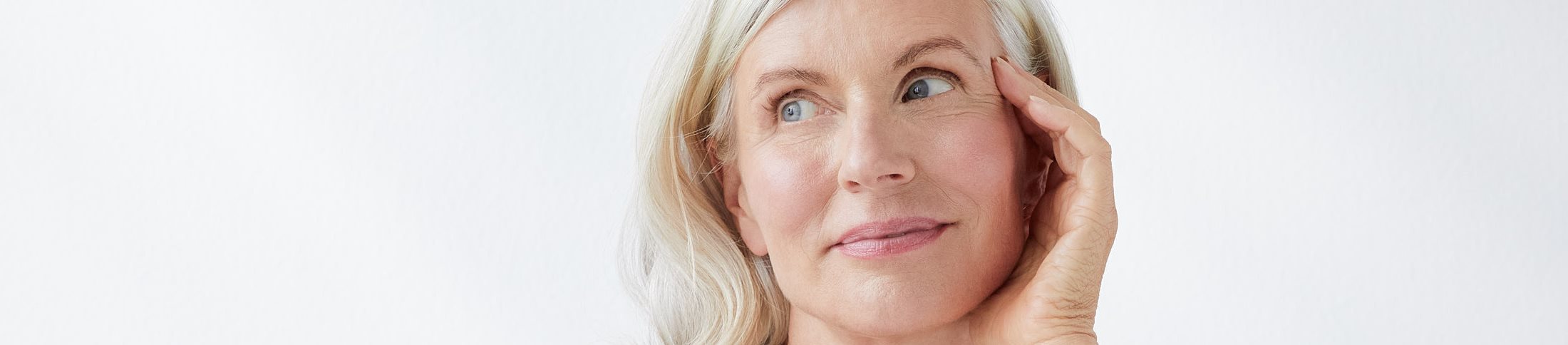 femme souriante qui se touche le visage, sur fond gris