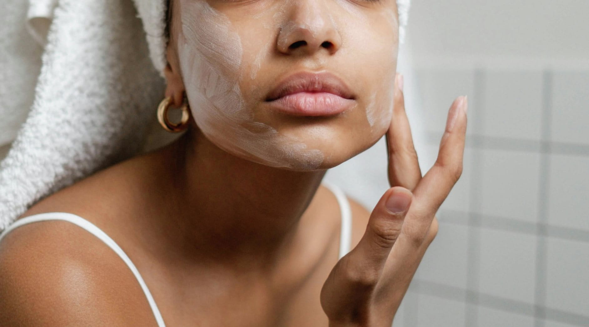 Mädchen mit Handtuch auf dem Kopf trägt Creme auf ihr Gesicht auf.