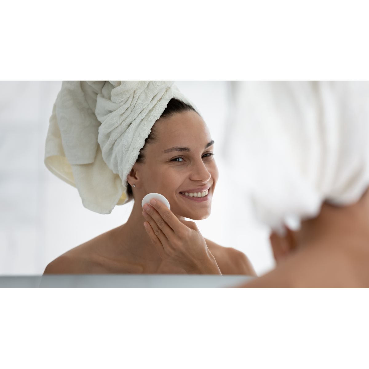 Frau wischt sich mit einem Wattepad über die Haut an der Wange.