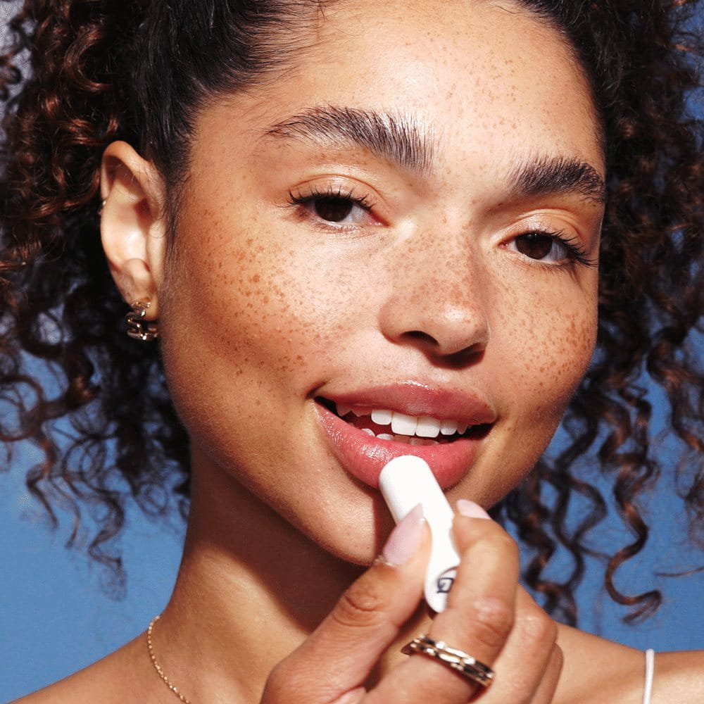 Woman smiling as she applies Aquaphor to her lips