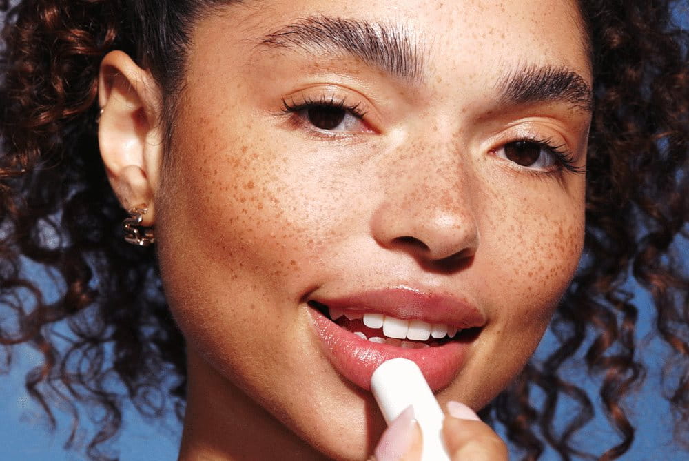 Woman smiling as she applies Aquaphor to her lips