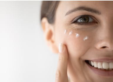 Nahaufnahme einer Frau mit straffer Haut, die mit einem Finger sanft ihr Gesicht berührt.