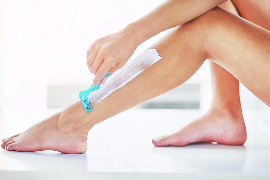 Donna che si rade le gambe con lametta e crema
