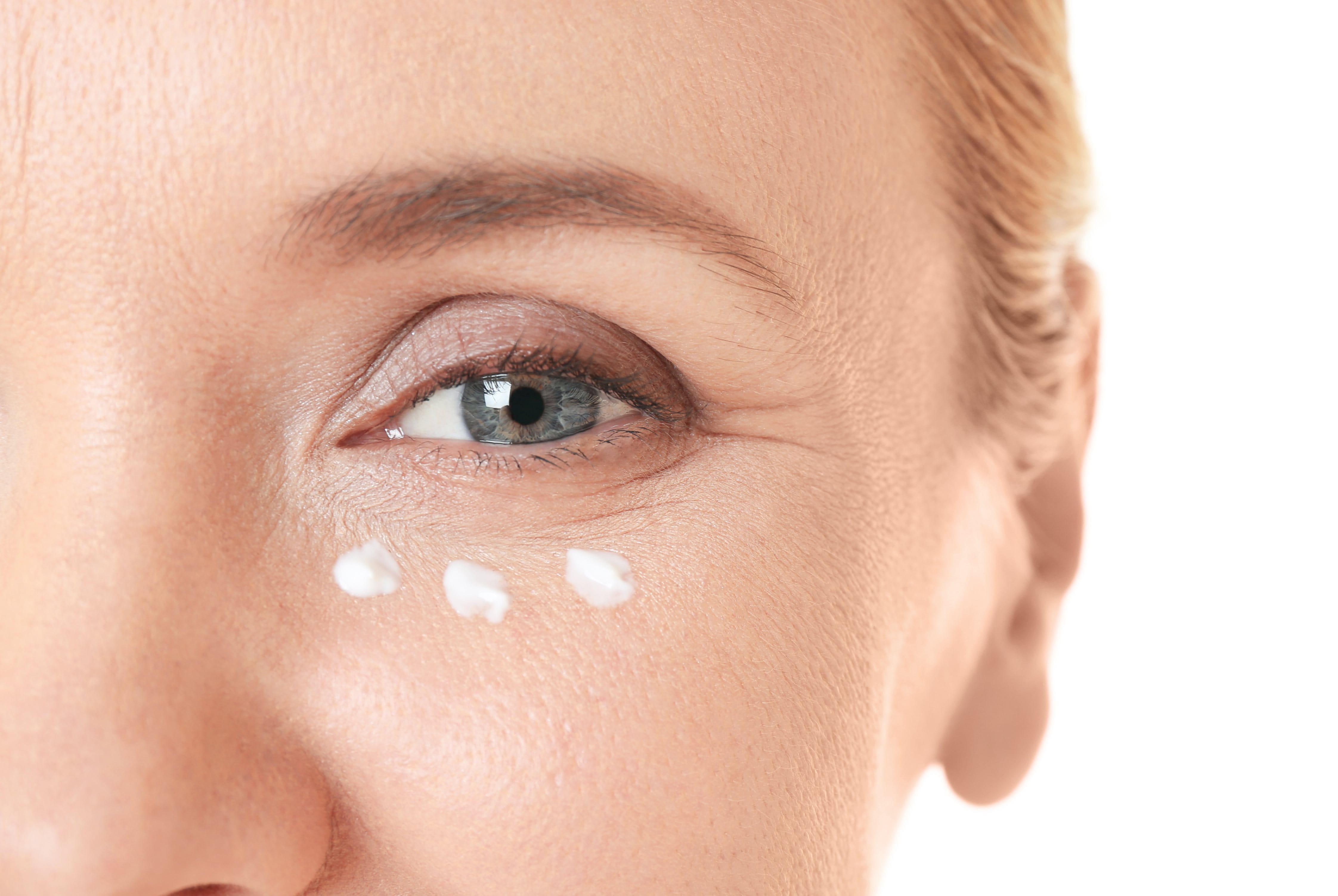 Nahaufnahme der Augenpartie einer blonden Frau. Unterhalb des Auges ist Creme zu sehen.