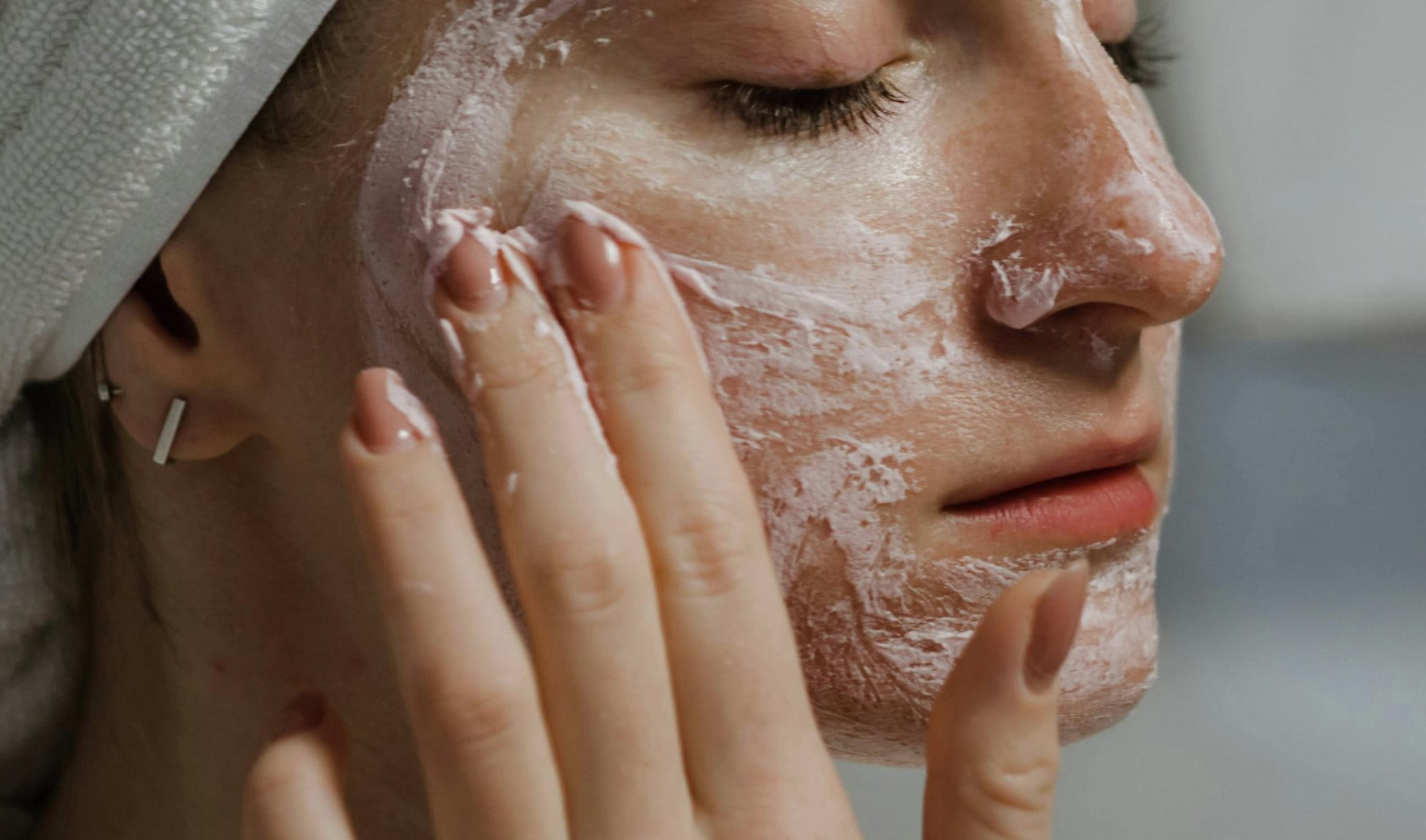 Frau mit gelben Handtuch auf dem Kopf trägt Peeling auf ihr Gesicht auf.