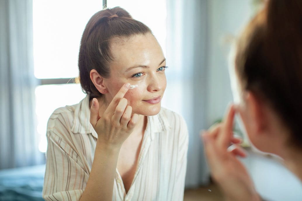 Donna applica crema contorno occhi ricca di peptidi davanti allo specchio durante una routine anti-età per pelle matura