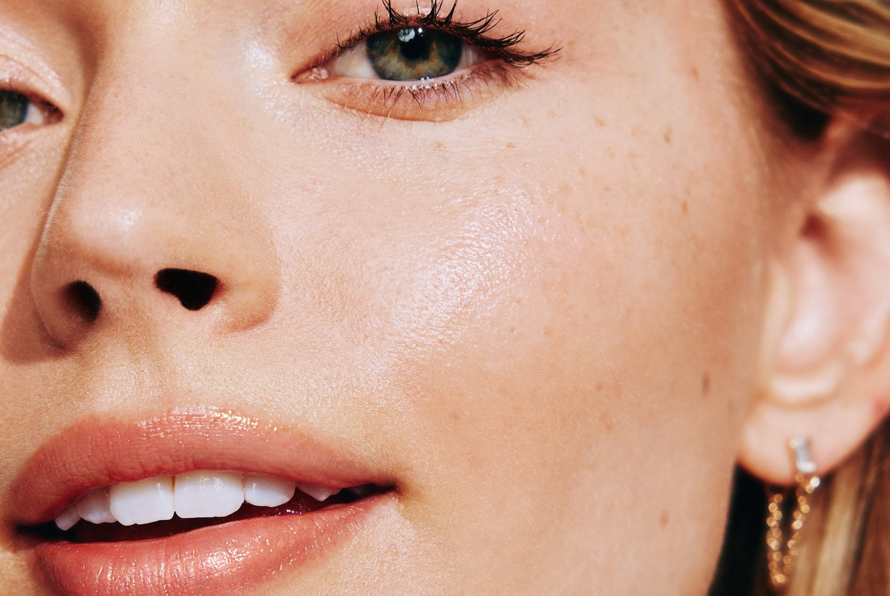 Close-up of a woman’s face showing freckles and smooth, radiant skin.