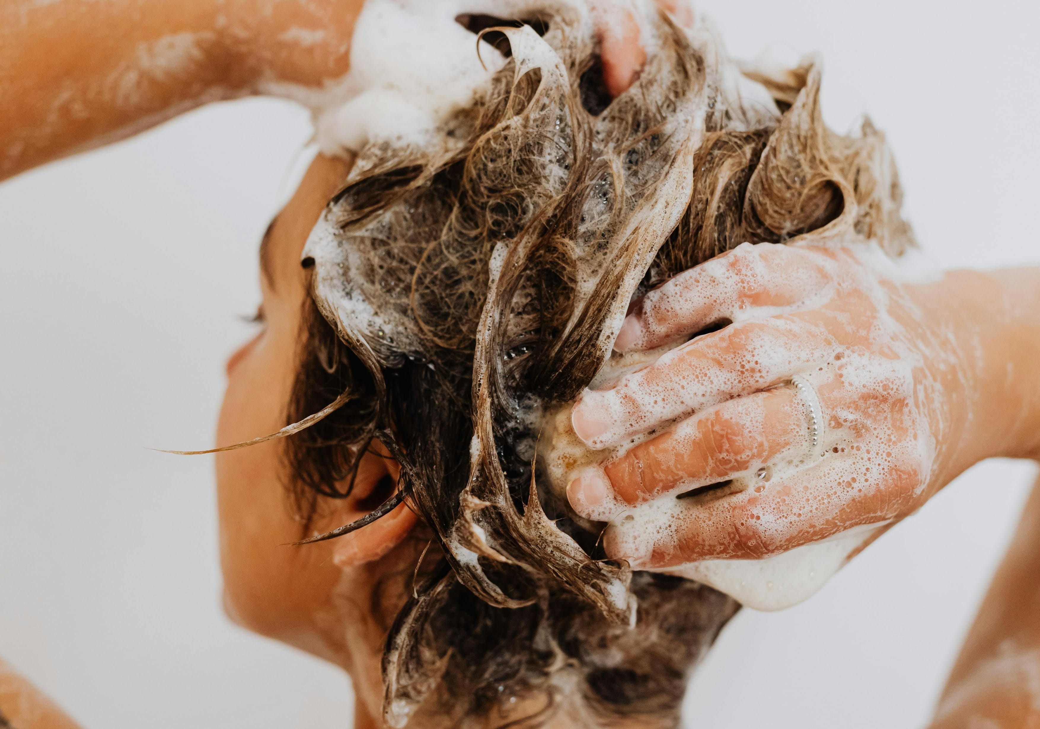 Rückenansicht einer Frau, die sich die Haare mit Shampoo wäscht.
