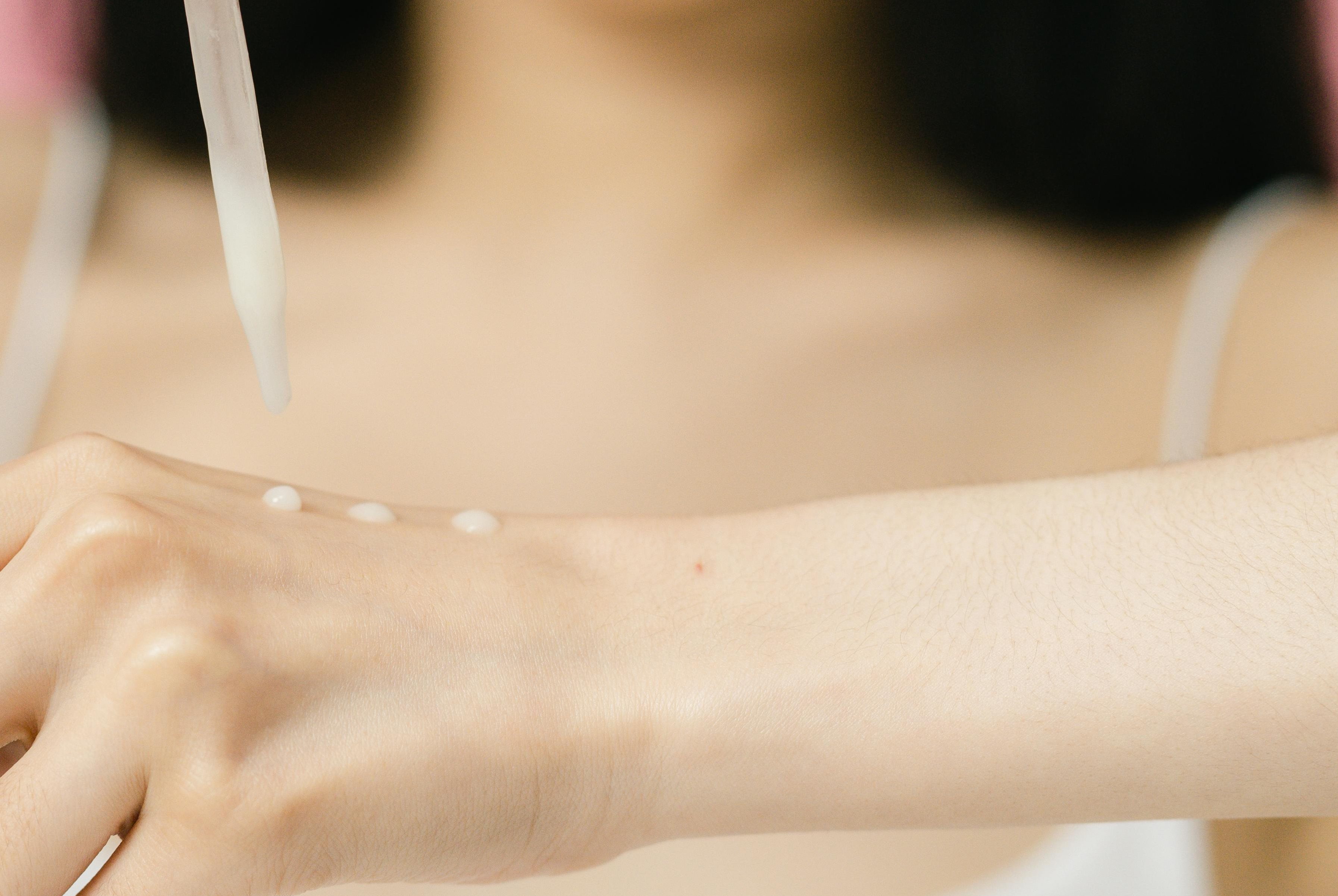 Nahaufnahme einer Frau, die sich mithilfe einer Pinzette ein weißes Serum auf den Handrücken tropft.