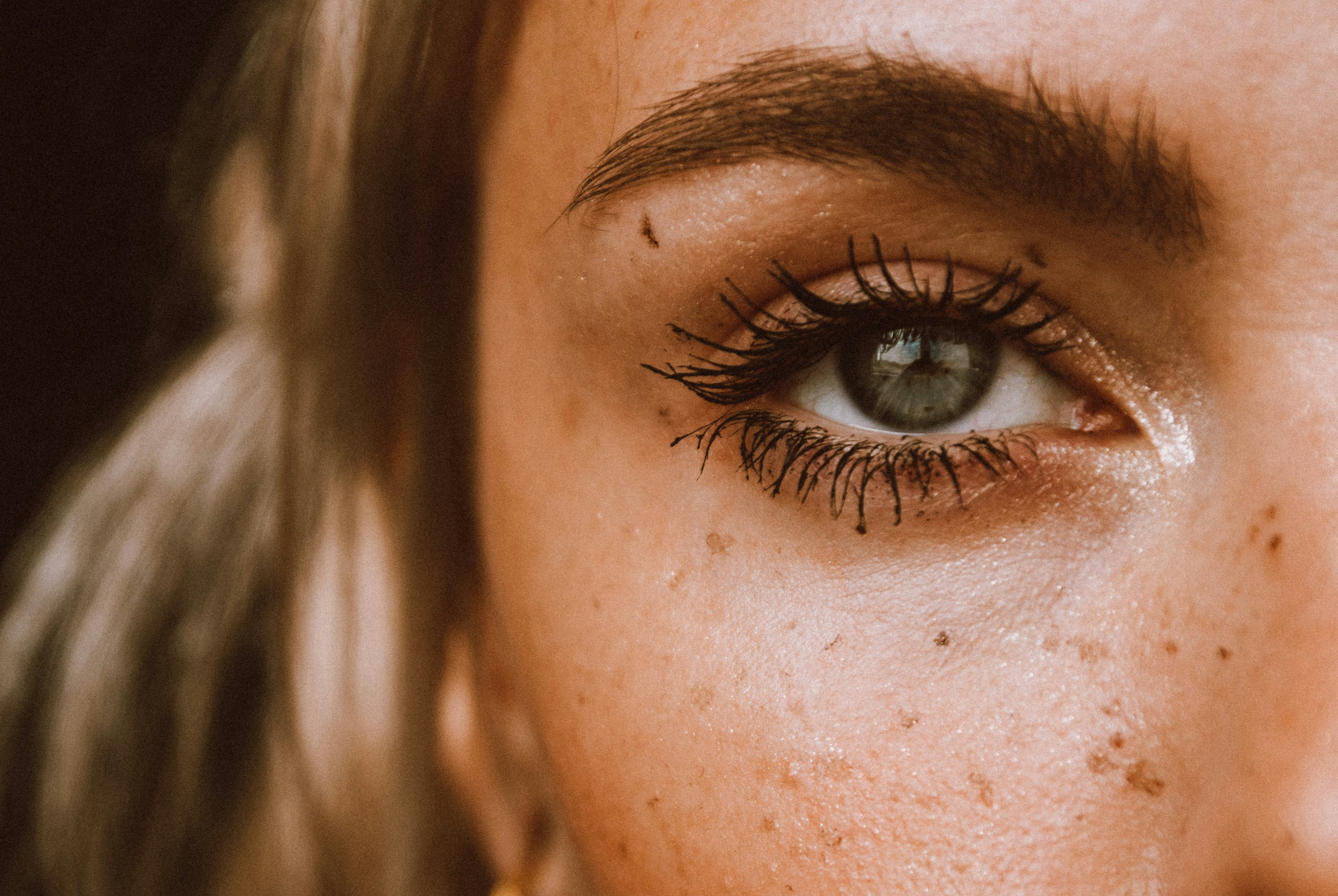 Nahaufnahme der linken Gesichtshälfte einer jungen kaukasischen Frau mit kleinen Pigmentflecken im Bereich der Augenpartie