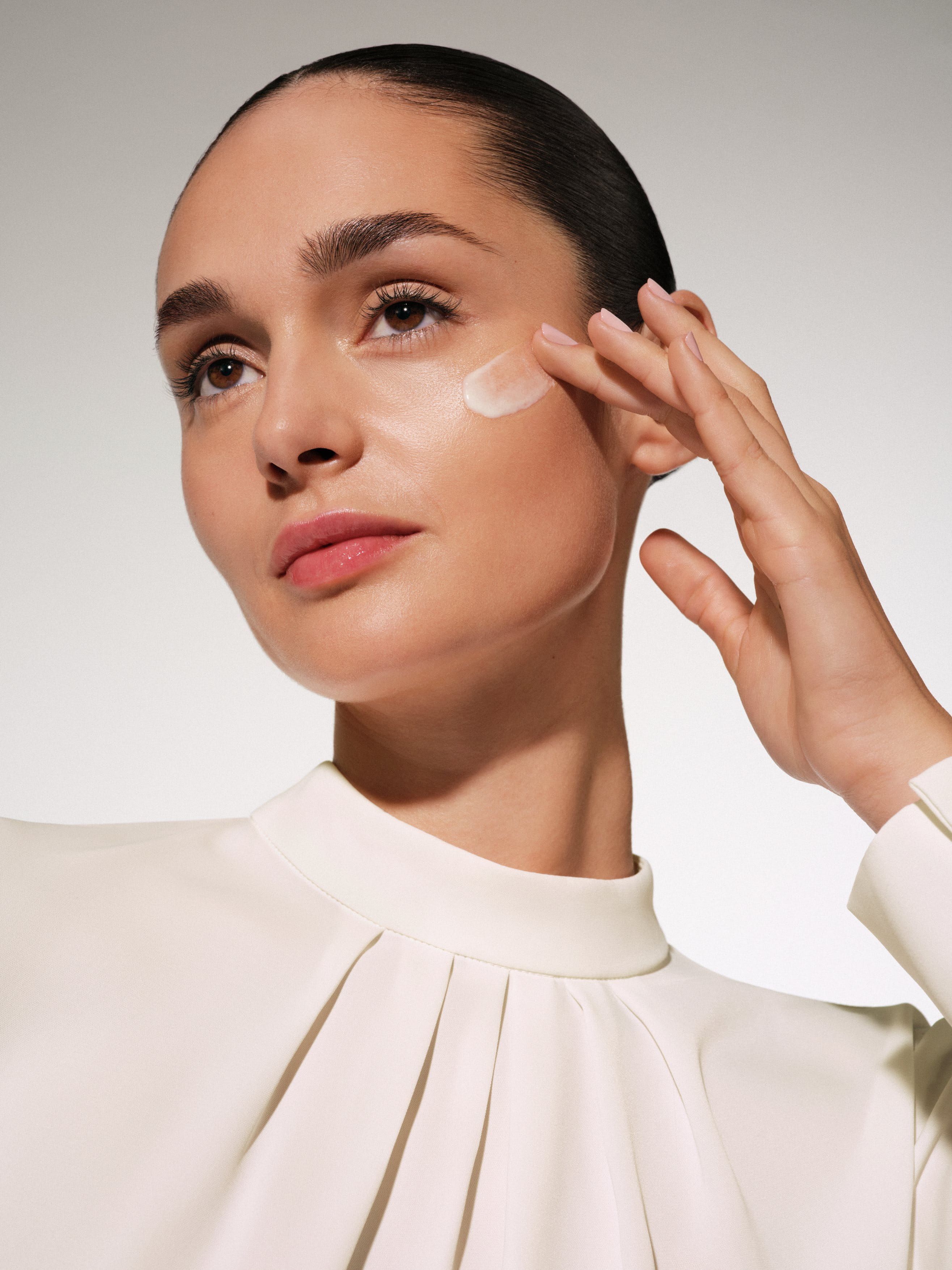 Mujer aplicándose protector solar facial con color, mostrando un tono de piel uniforme y protección contra los rayos UV. 