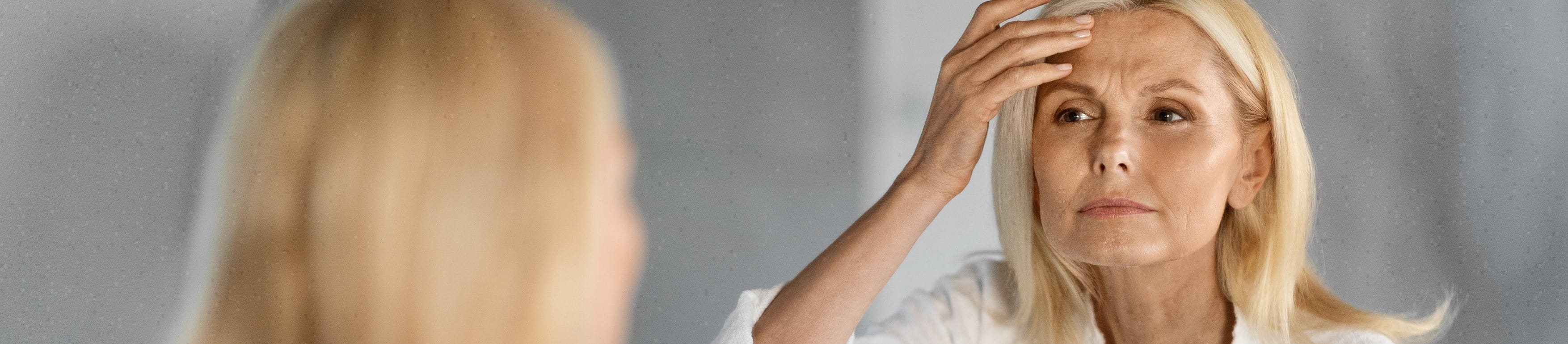 Frau vor dem Spiegel mit sichtbaren Stirn- und Zornesfalten.