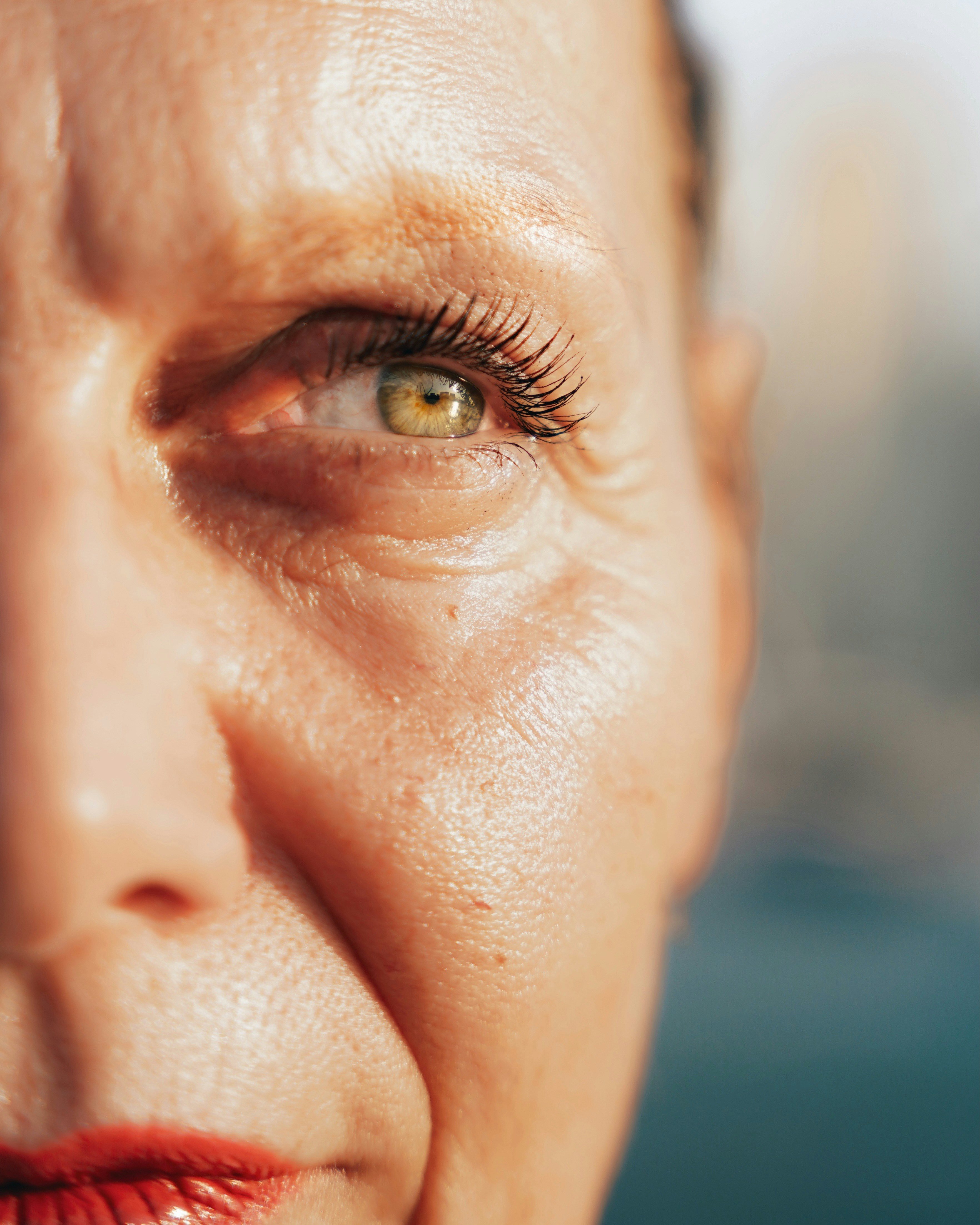 Nahaufnahme der rechten Gesichtshälfte einer Frau mit heller Haut, die in der Sonne steht. Ihre dünner werdende Haut zeigt feine Linien und Falten.