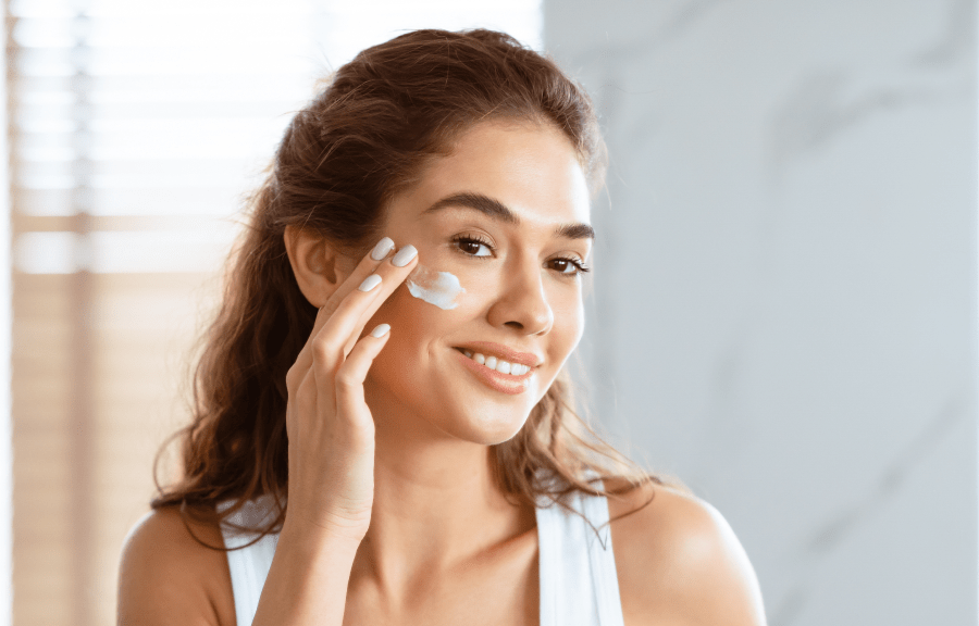 Vrouw brengt verzorgingscrème aan op haar wangen als voorbereiding op make-up bij acnegevoelige huid.