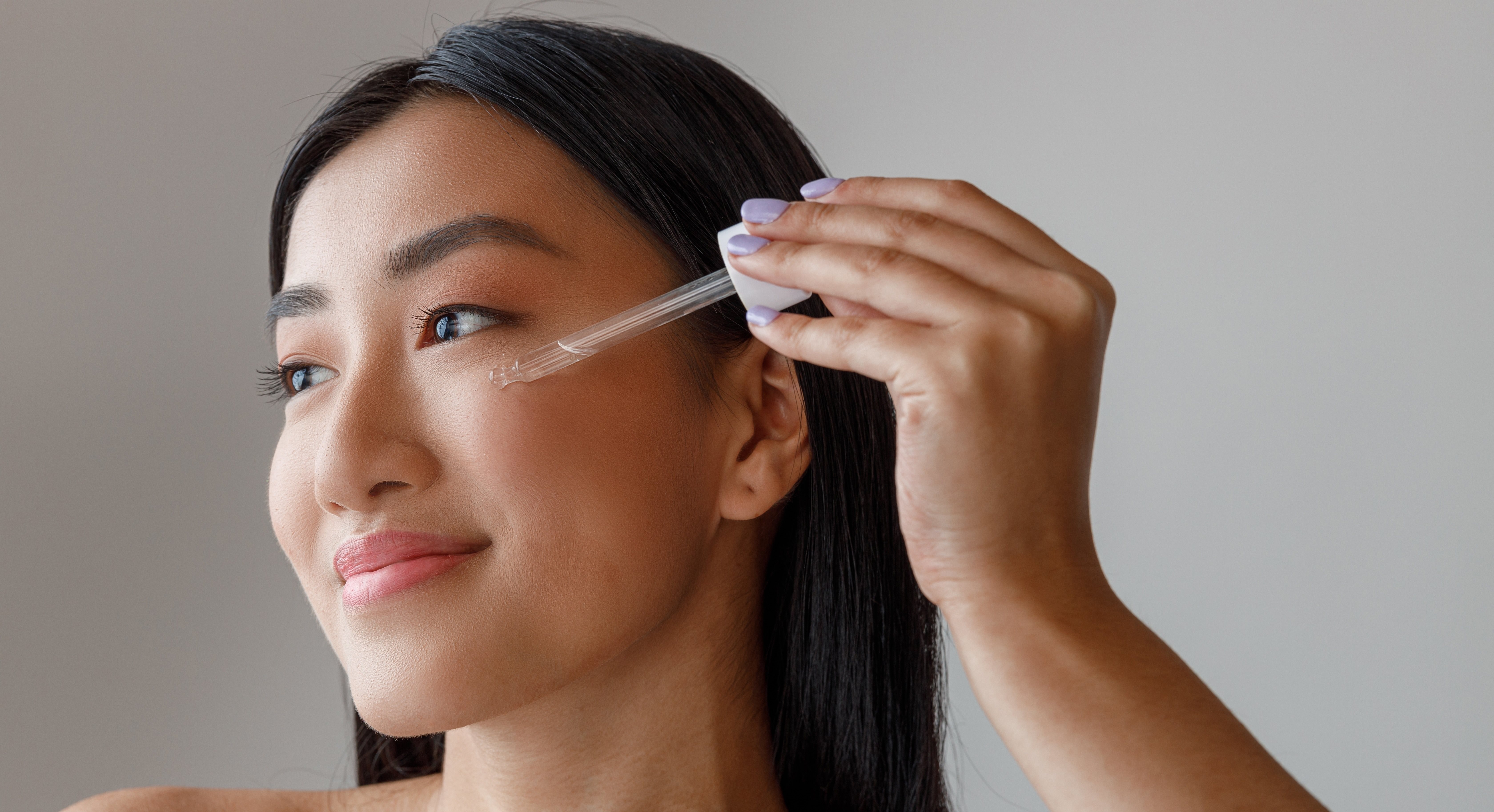 Junge Frau, die sich ein feuchtigkeitsspendendes Serum mit einer Pipette auf dem Gesicht aufträgt