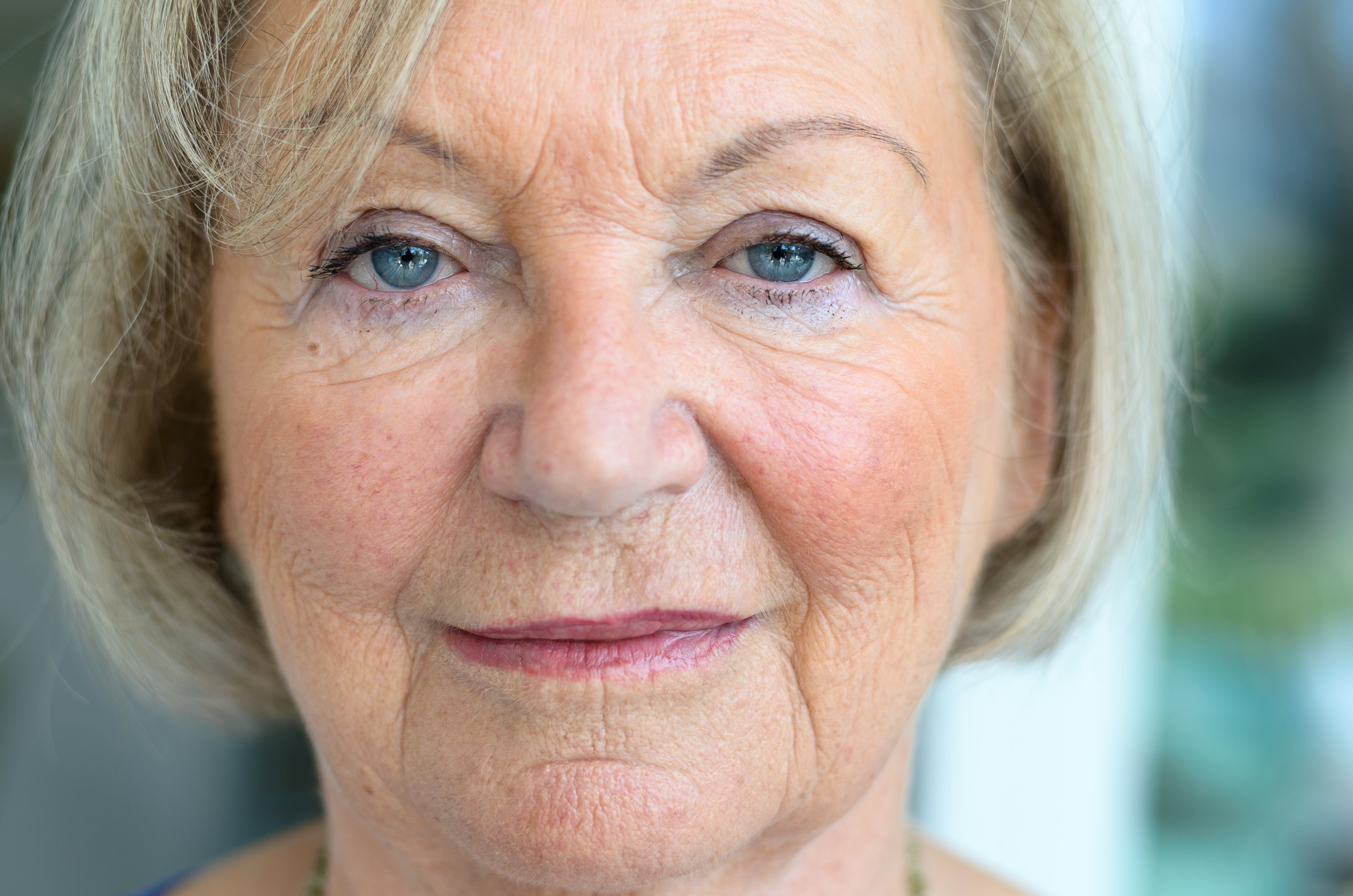 Eine ältere Frau mit Falten blickt mit strengem Blick frontal in die Kamera.