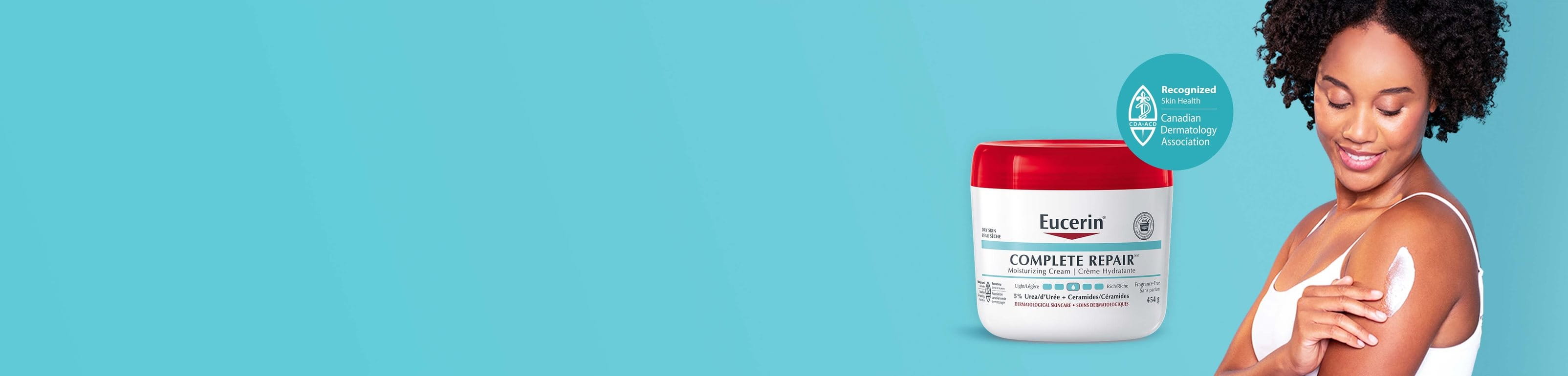 View of a female model wearing a white tank top and sitting down with her knees bent with the Eucerin Complete Repair 454g product in the background.