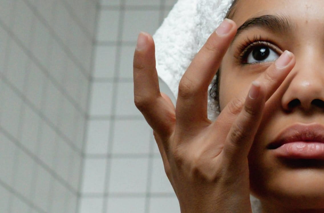 Mädchen trägt sich mit einem Finger sanft Pflege unter ihrem Auge auf.