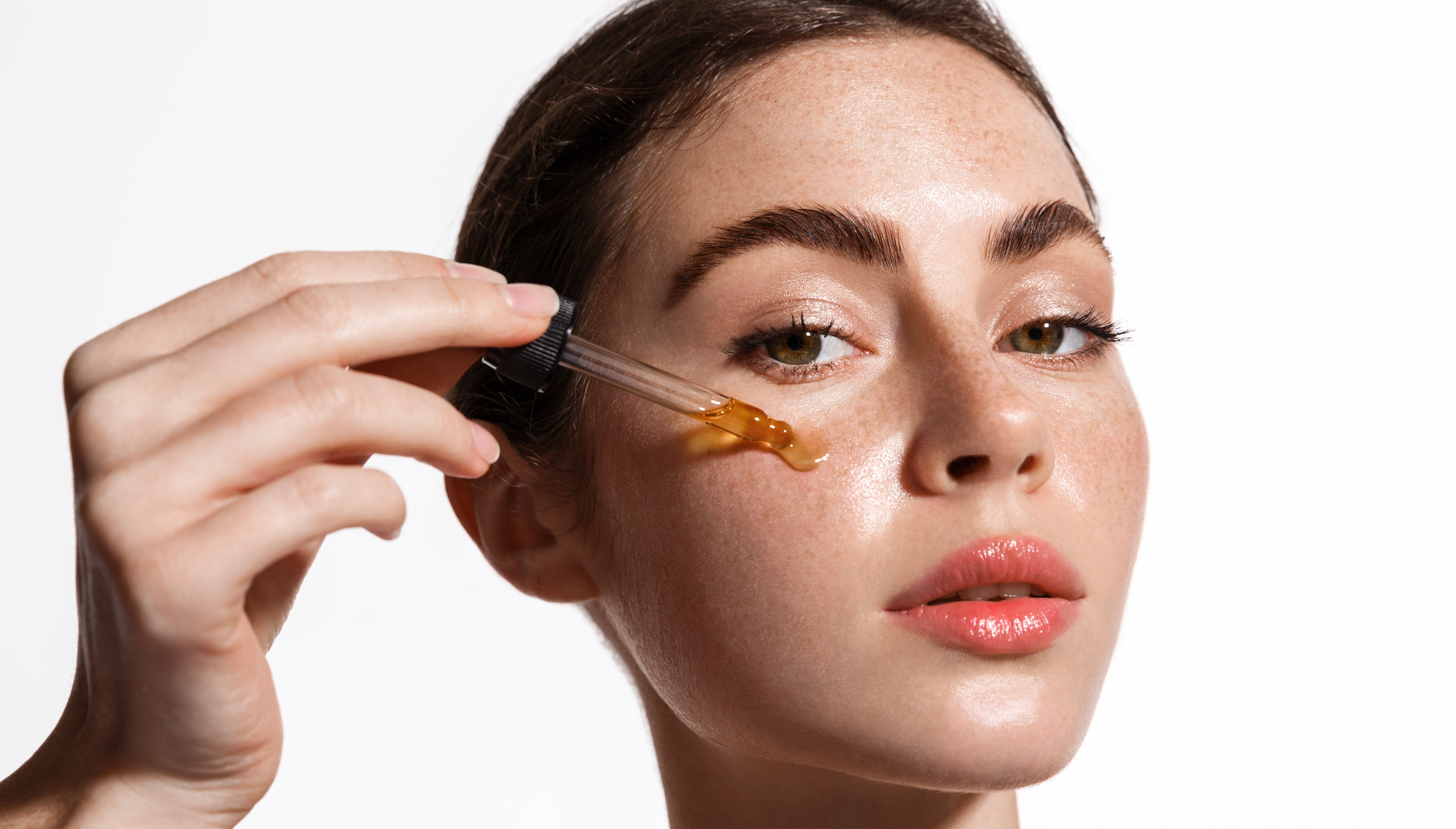 Eine Frau trägt ein Öl mit einer Pipette auf ihre Wange auf.