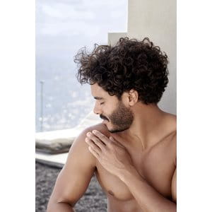 immagine di un uomo che si spalma la crema solare sulla spalla mentre è in spiaggia