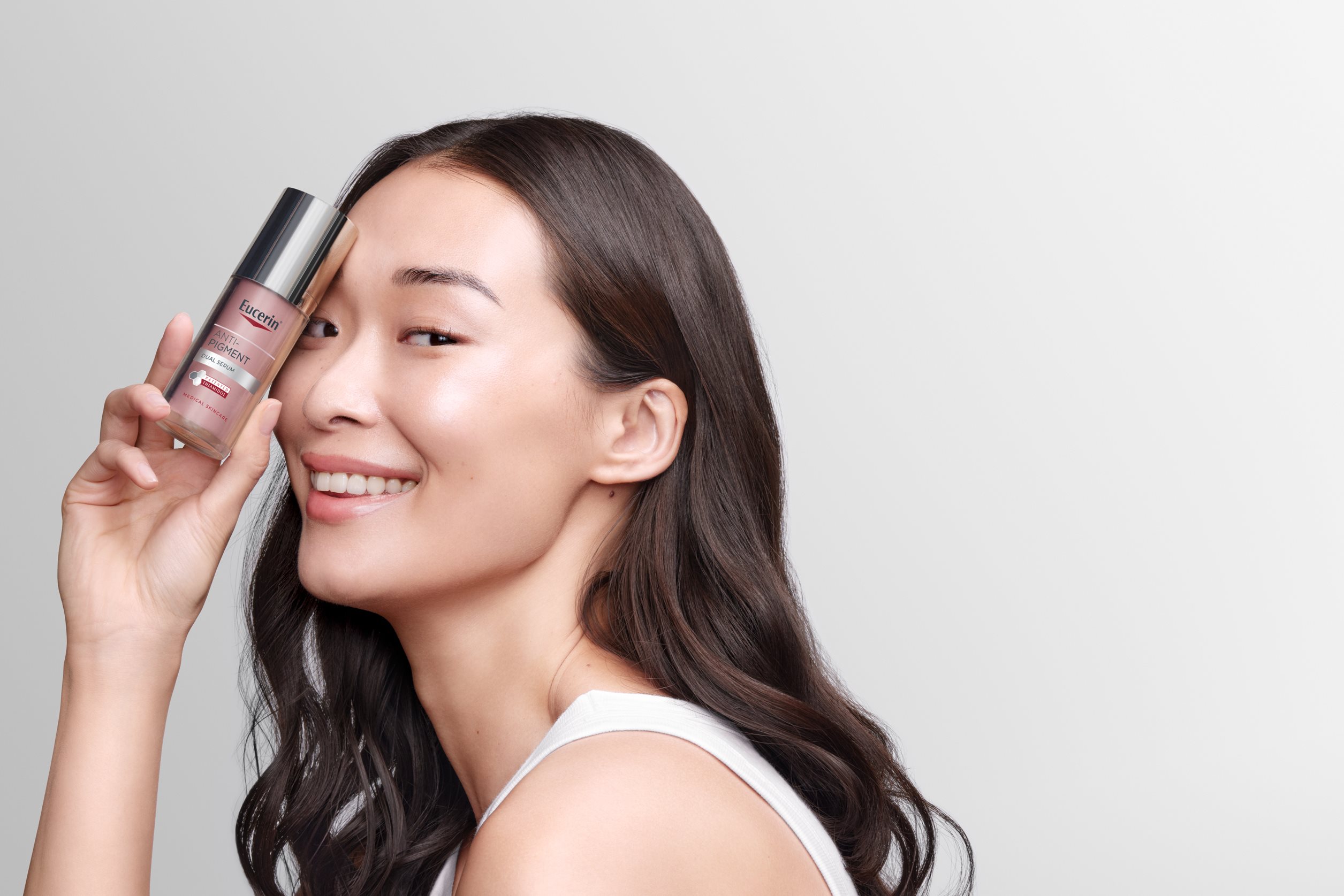 A picture of a woman with glass skin holding an Anti pigment dual serum